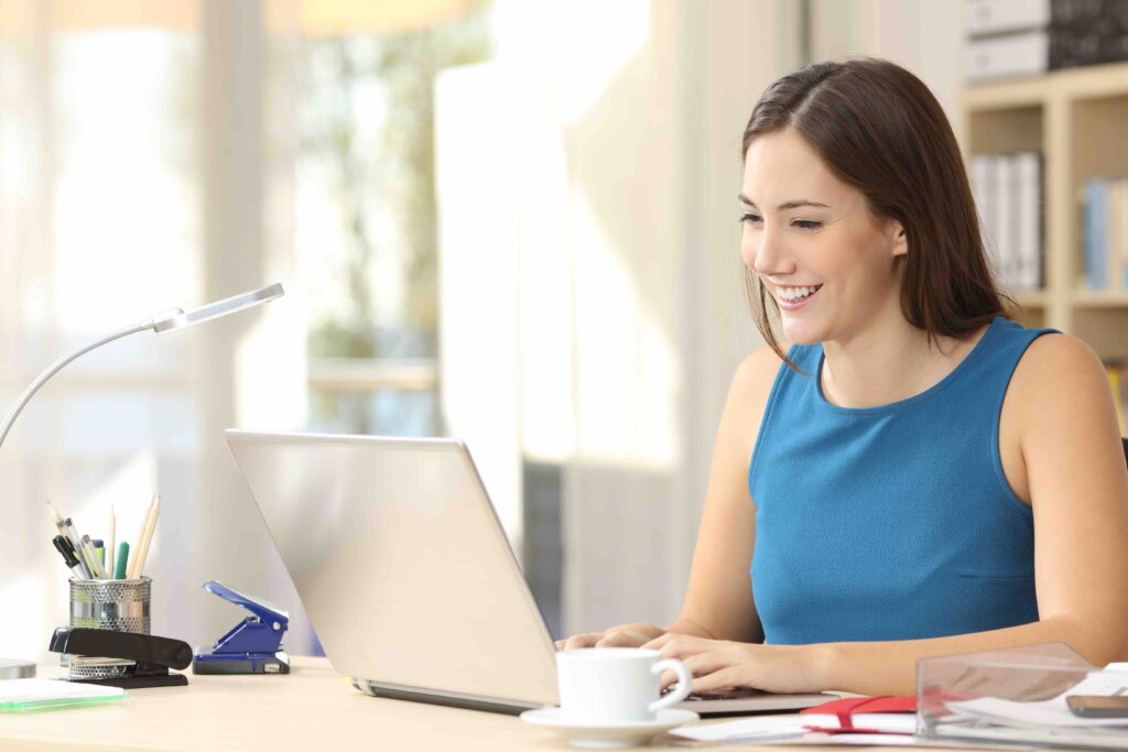 Happy casual entrepreneur working on line typing with a laptop at office with a window in the background